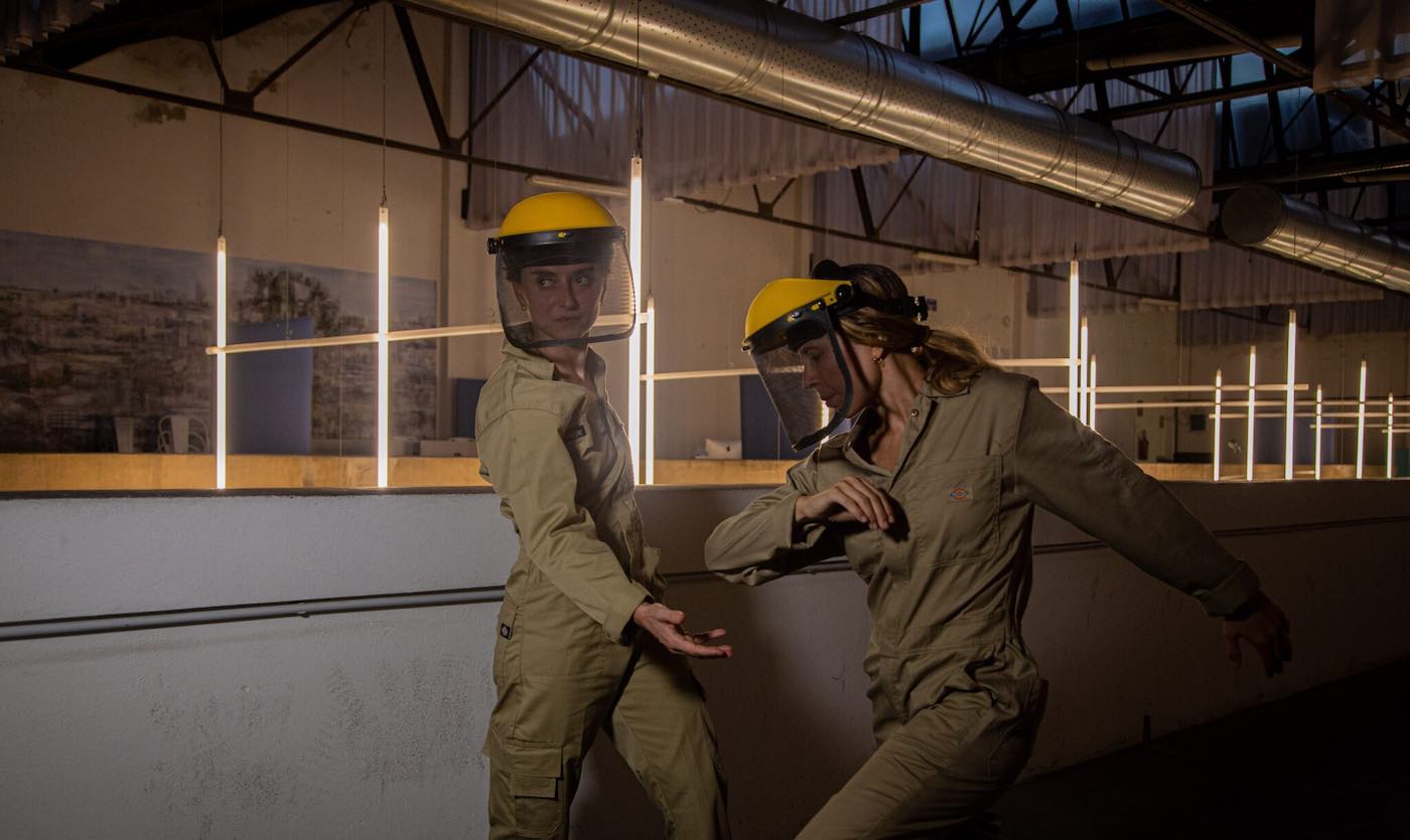 Two people in construction work clothing in an industrial building.